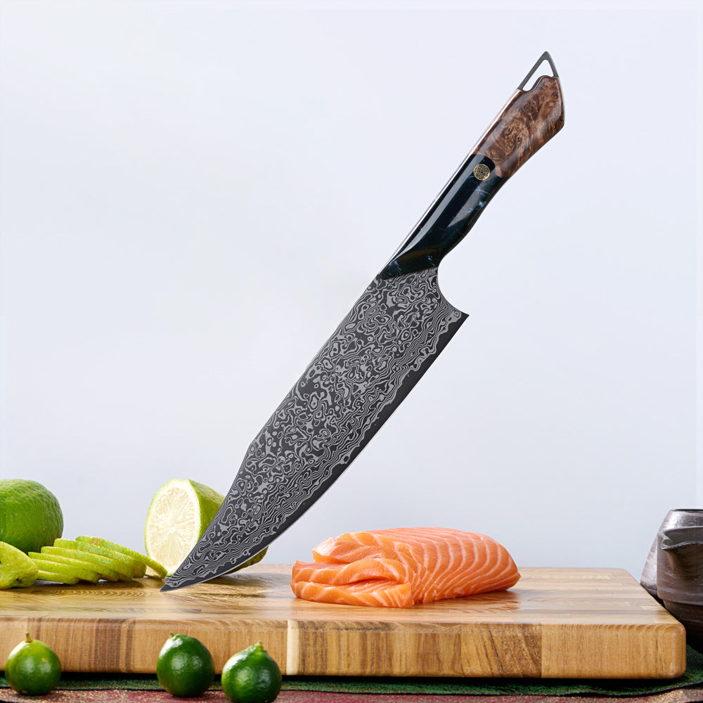 A large chef's knife with a patterned Damascus-style steel blade and a brown wood handle, shown standing on a wooden cutting board with sliced salmon, limes, and cucumber props against a light gray background.