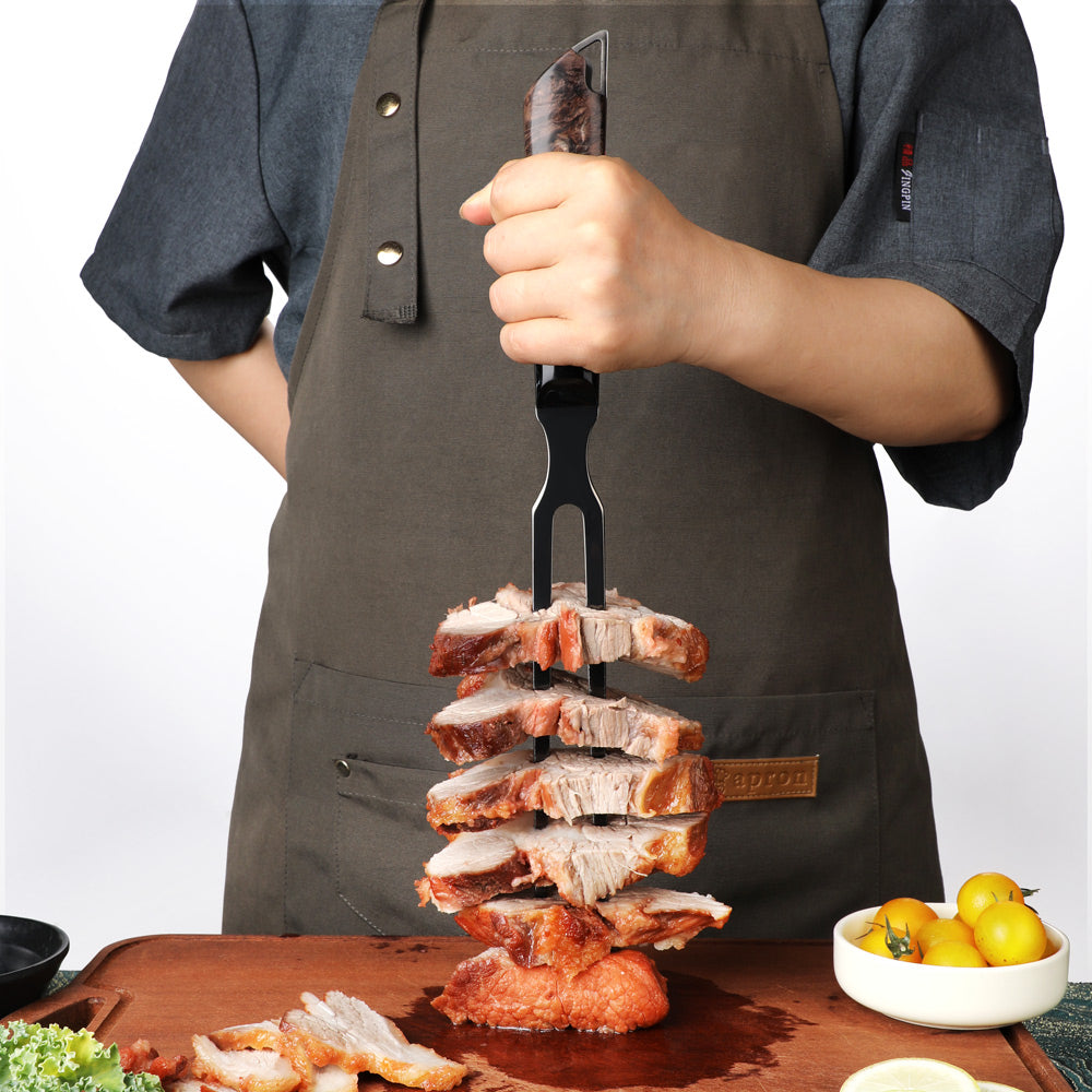 A person wearing a dark gray apron holds a black multi-pronged skewer tool loaded with stacked slices of cooked meat over a wooden cutting board, with small yellow tomatoes on a side.