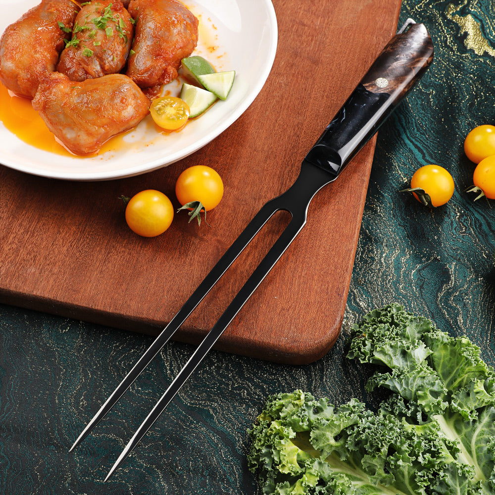 A black metal two-pronged fork with a polished dark handle rests diagonally on a wooden cutting board, surrounded by food props including chicken pieces, cherry tomatoes, kale, and a white plate on a dark textured surface.