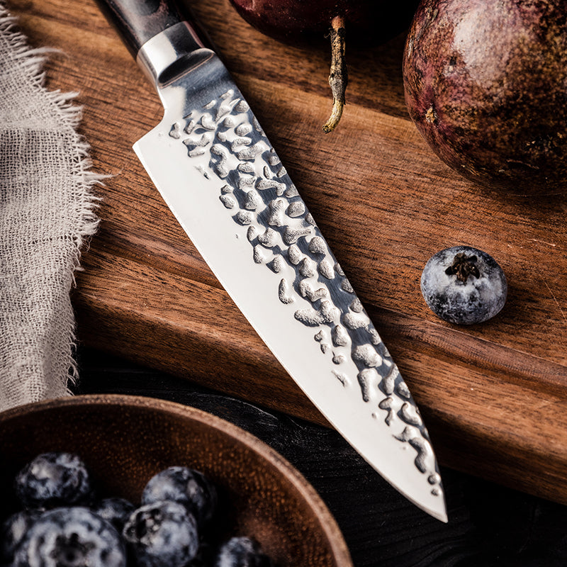 Professional small Japanese knife stainless steel blade hammered  on a wooden cutting board with fruits and a bowl of blueberries.