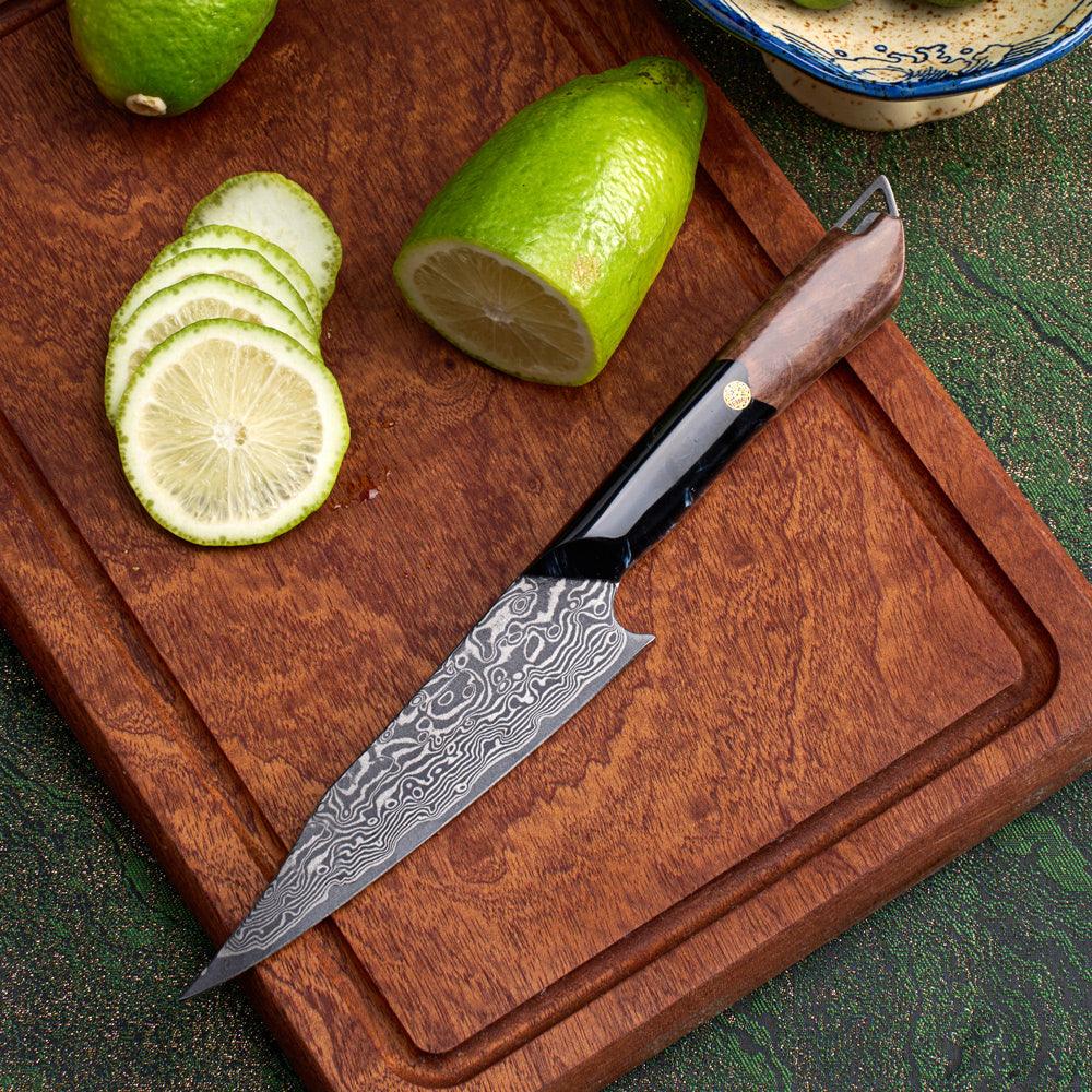 A Japanese-style kitchen knife with a Damascus steel blade and a brown wooden handle, resting on a wooden cutting board with sliced and whole limes.