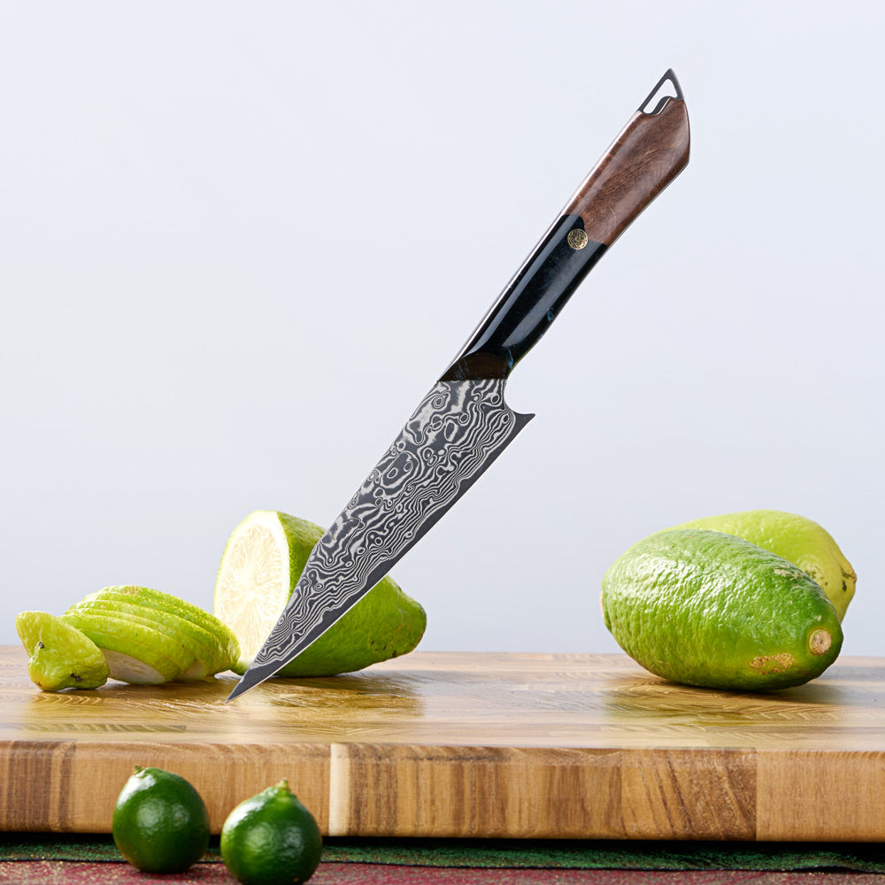 A kitchen knife with a patterned Damascus steel blade and a dark brown wooden handle, shown standing on a wooden cutting board with limes around it against a light gray background.